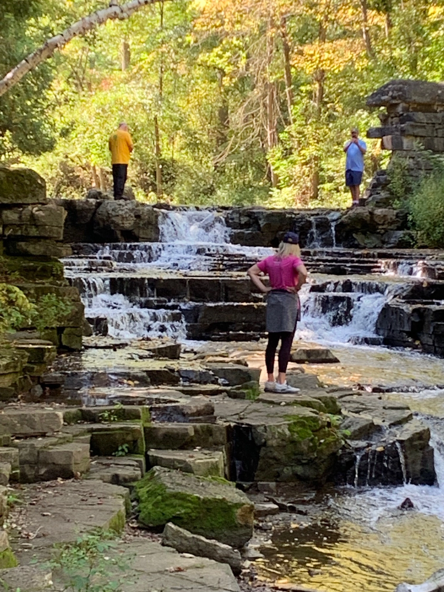 Pilgrims exploring a stepped waterfall and rock ledges in an autumn wood