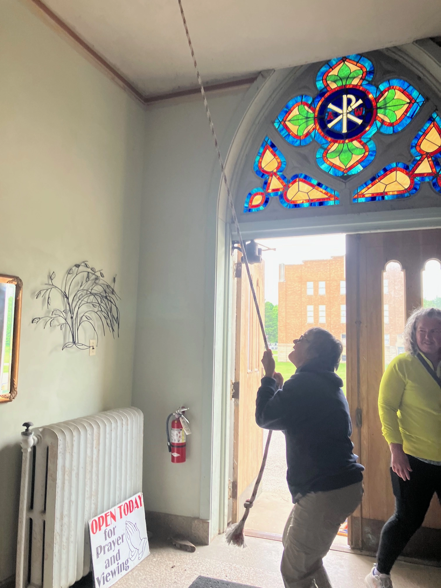 A pilgrim ringing a church bell by its rope, beneath a stained glass window
