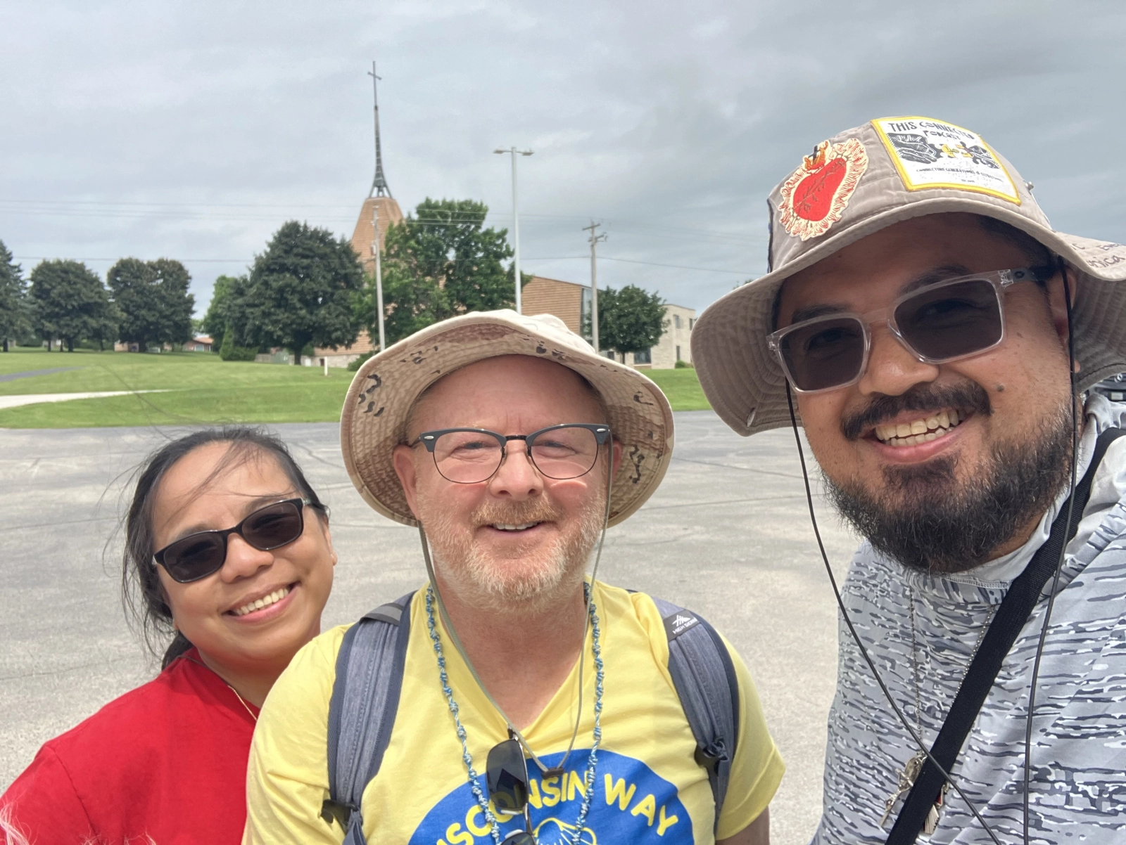 Three smiling pilgrims taking a selfie, with a church steeple behind them