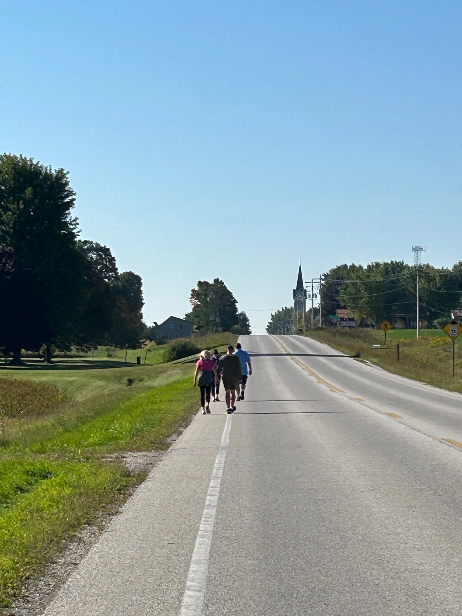 Pilgrims walking along a country road toward a distant church steeple