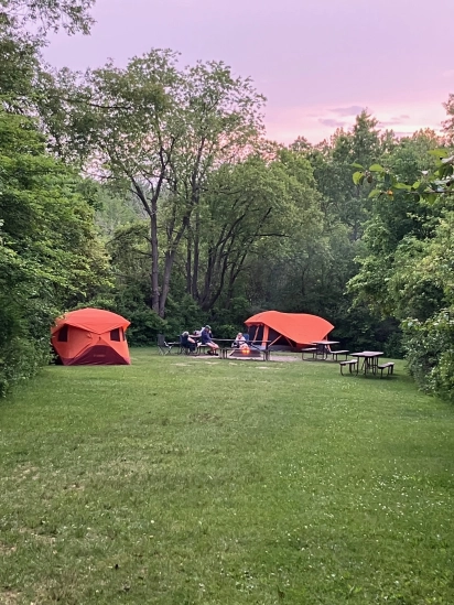 Orange camp tents pitched in a grassy clearing at dusk