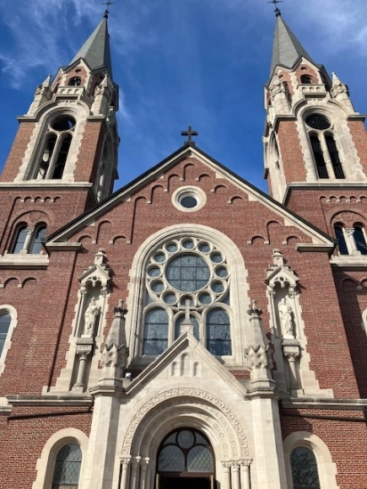 The twin red brick spires of a Gothic church against a blue sky